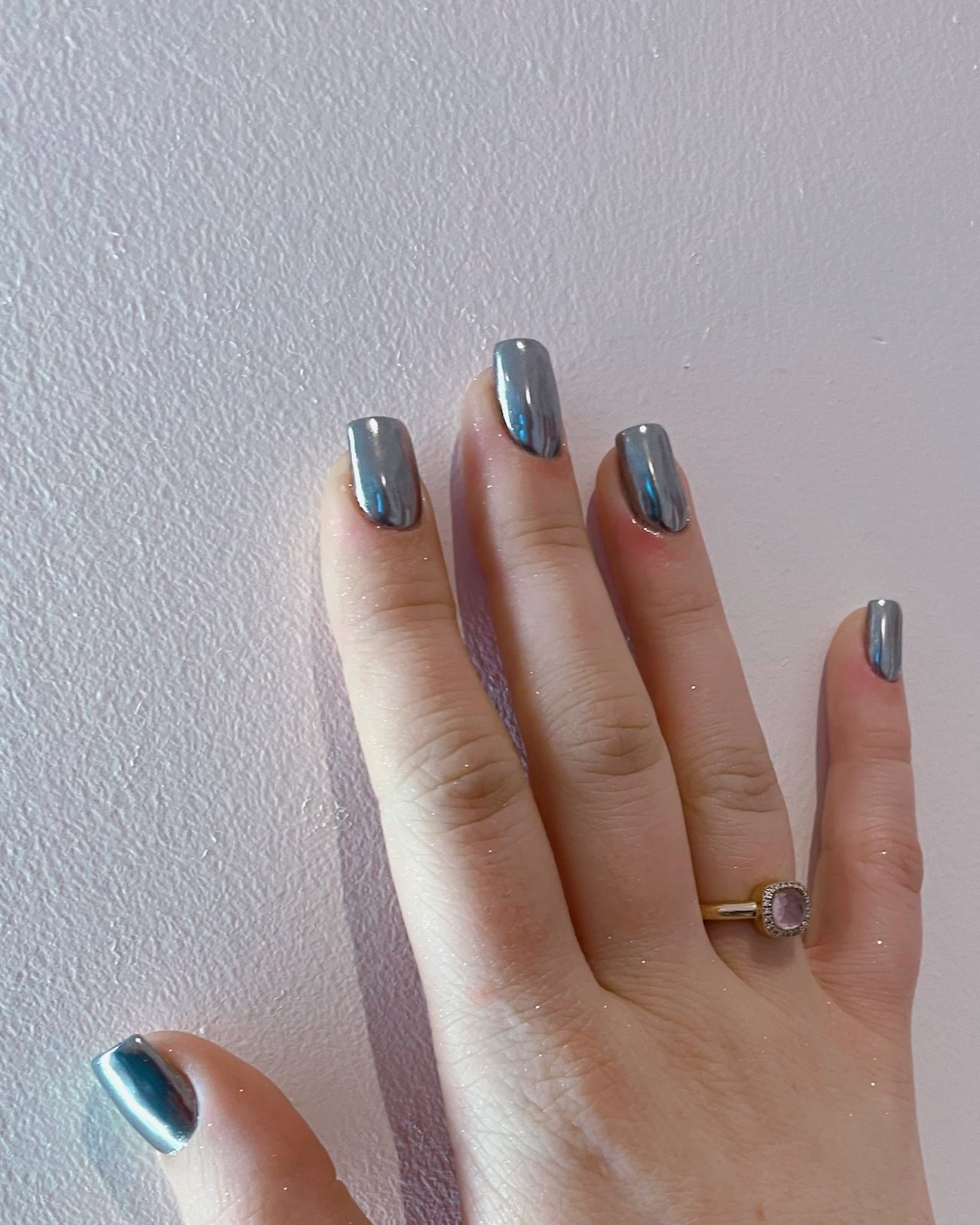 Grijze chrome nagels, een hand tegen een lichte muur