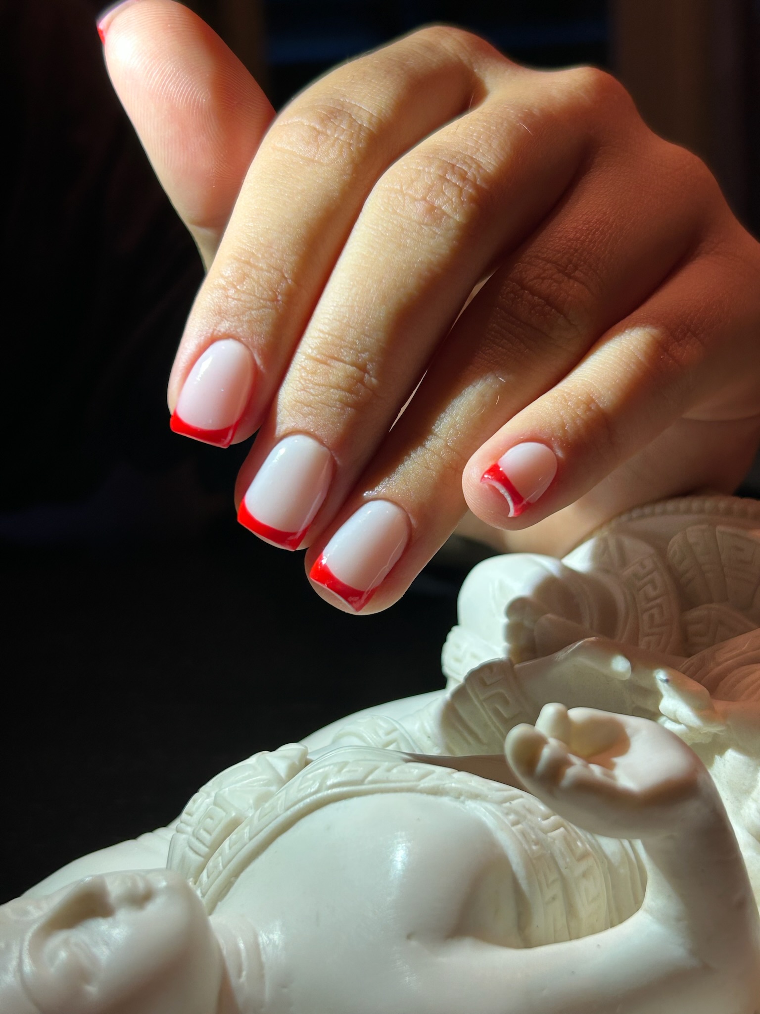 Witte nagels met rode French randjes naast een wit beeldje