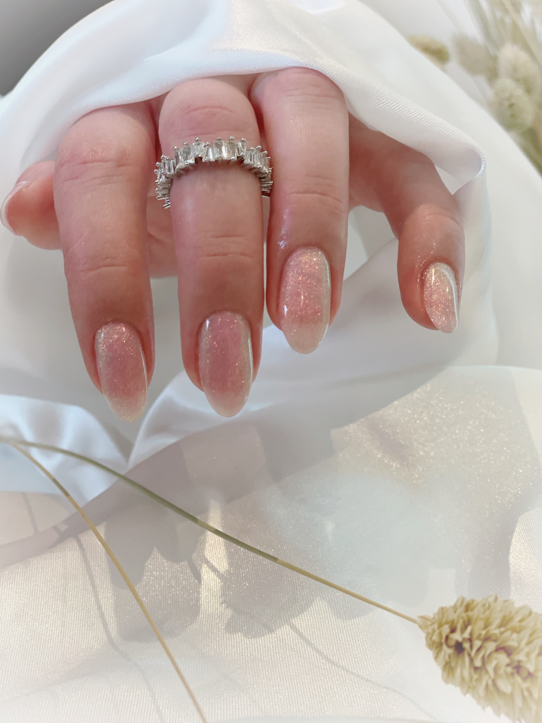 Nude nagels met glitter op witte stof met droogbloemen