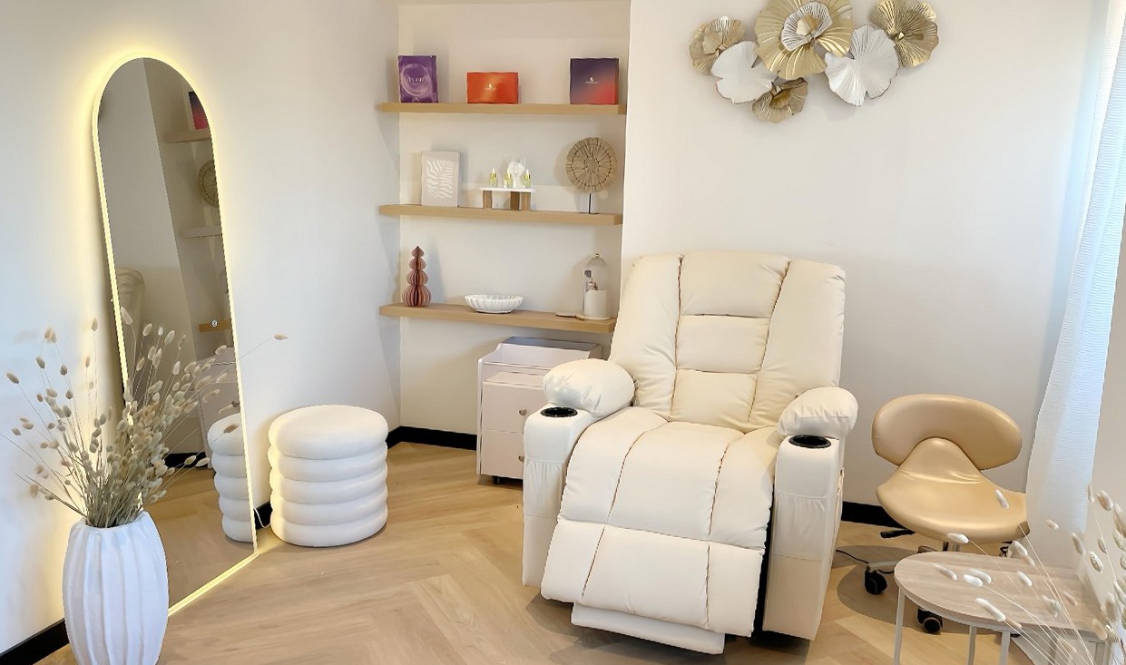 De behandelhoek: een crèmekleurige massagestoel, een verlichte boogspiegel en gouden bloemen aan de muur