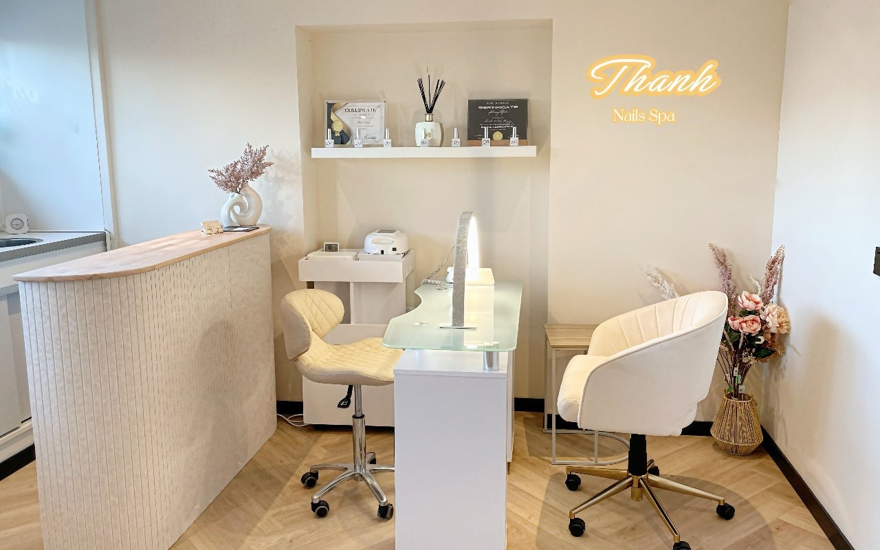De manicuretafel met witte stoelen, een geribbelde ronde balie en het neonbord Thanh Nails Spa